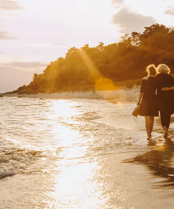 Par går ved siden af hinanden i vandkanten på stranden ved solnedgang